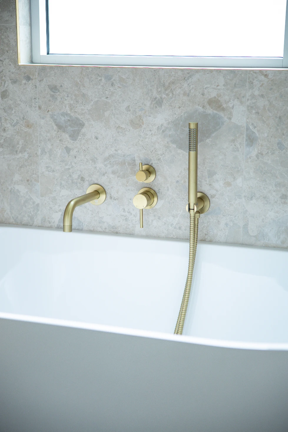 Bath edge in profile — brushed brass against Norrock Ivory's soft stone tones.