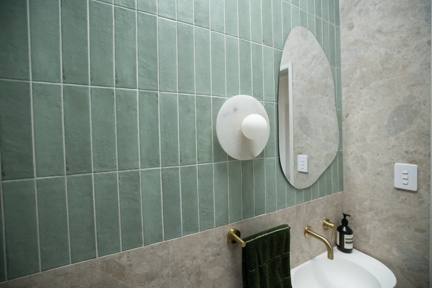 Powder room — the customer's green Zellige vertical-stacked across the upper walls, Norrock Ivory below, brushed brass and marble as the soft accents.