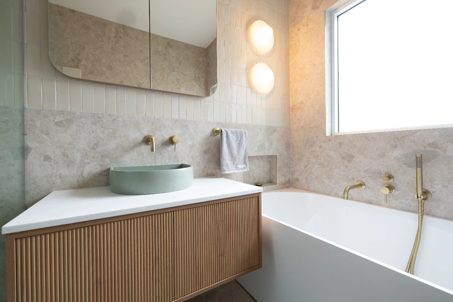 Main bathroom — Norrock Ivory porcelain with a Zellige Natural feature wall, mint basin on a fluted timber vanity, and brushed brass tapware throughout.