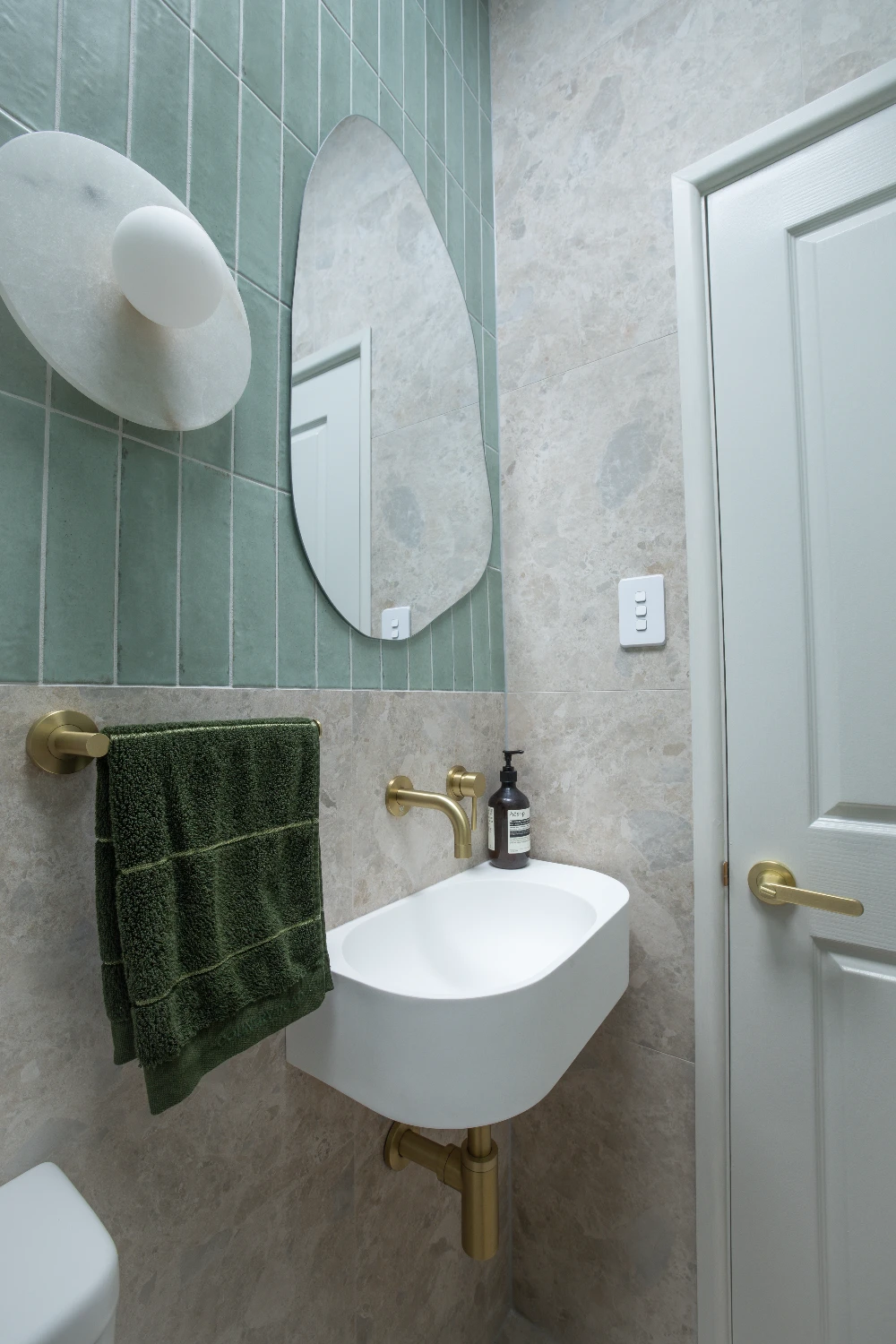 Sink detail — the white wall-hung basin and brushed brass tap against the green Zellige.